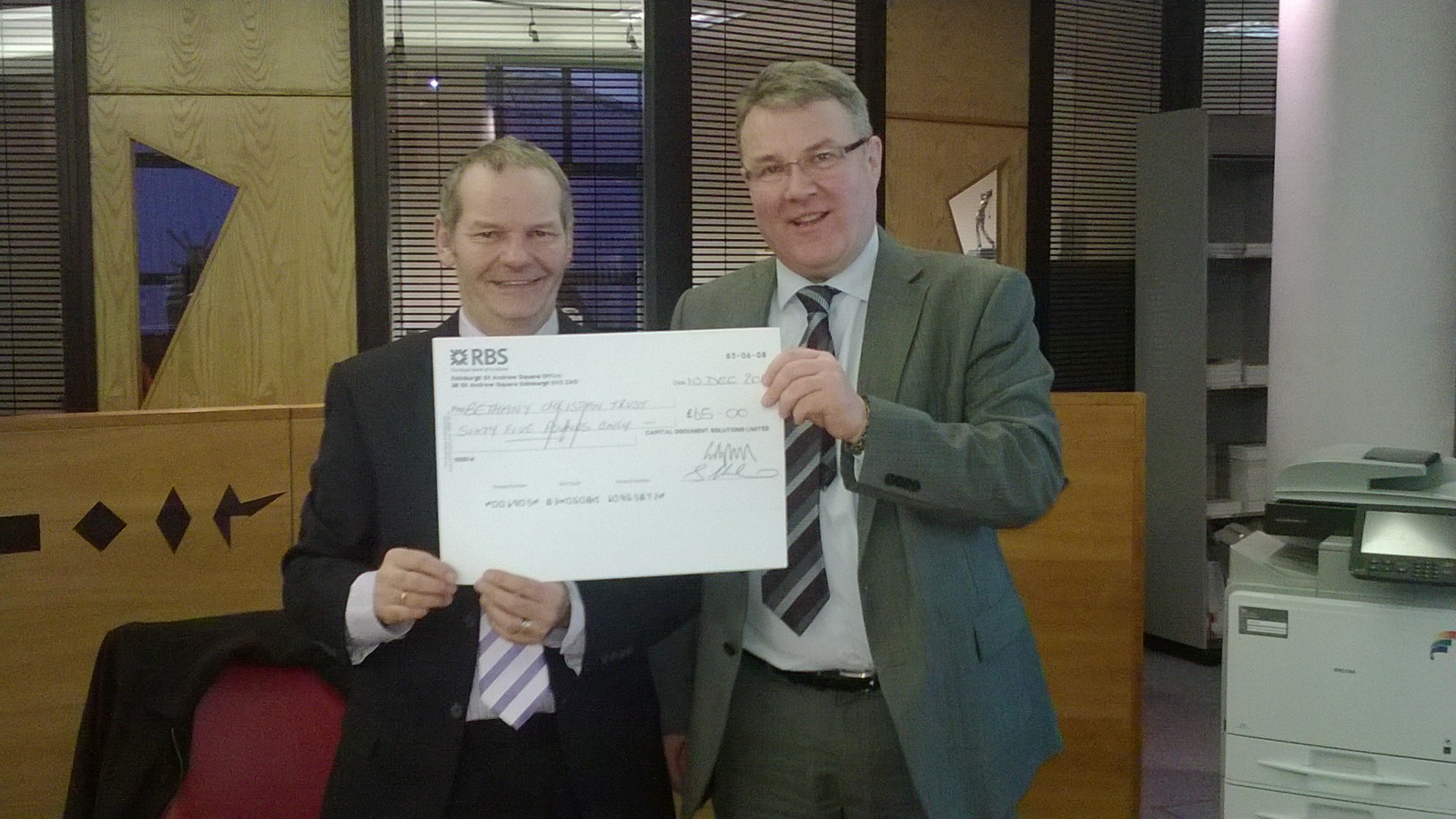 Ross Whailin of Bethany Christian Trust receives a donation from Mark Harvie of Capital